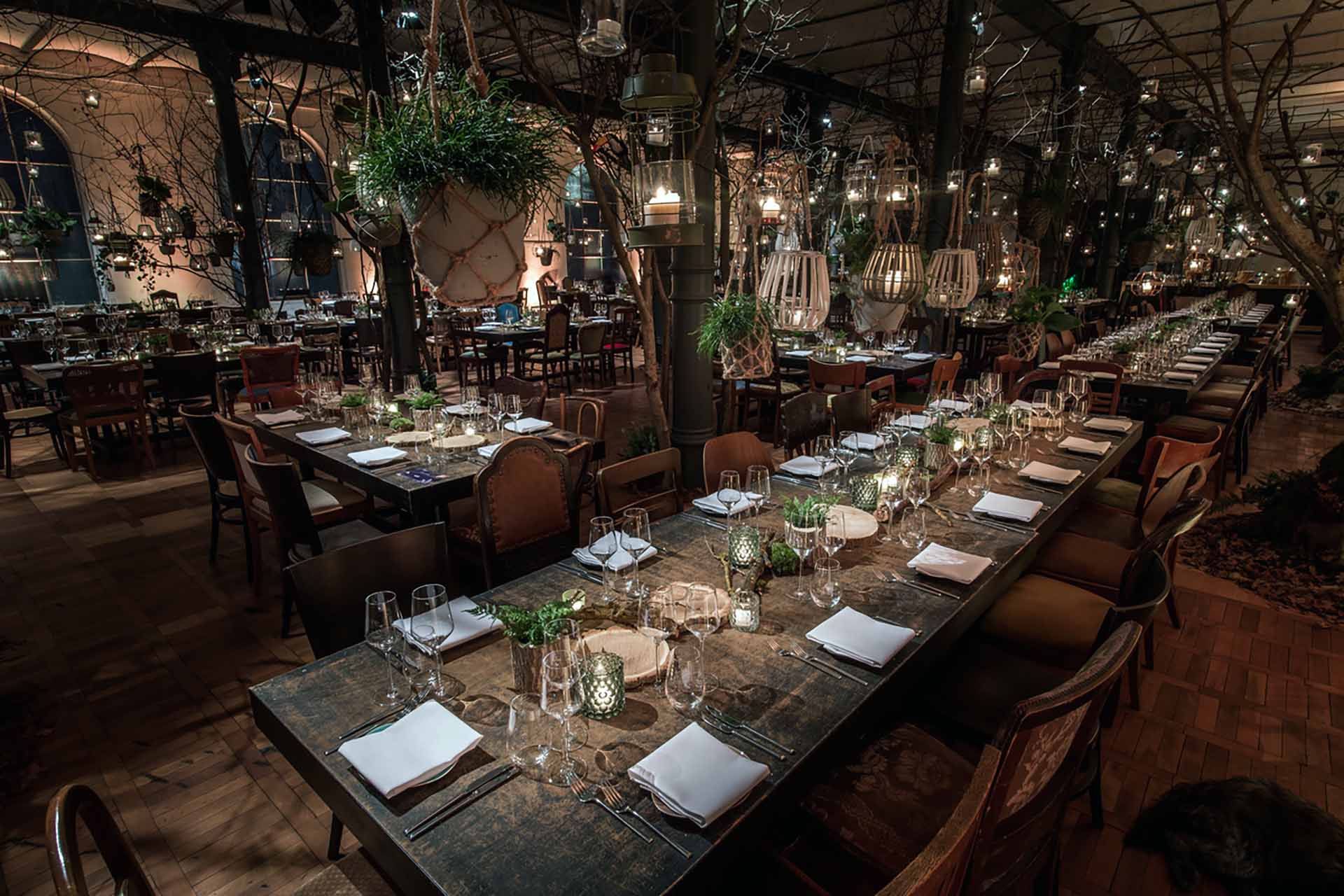 Corporate events management Berlin – elegantly set banquet tables in an enchanted forest concept with lanterns and plants at the Heeresbäckerei