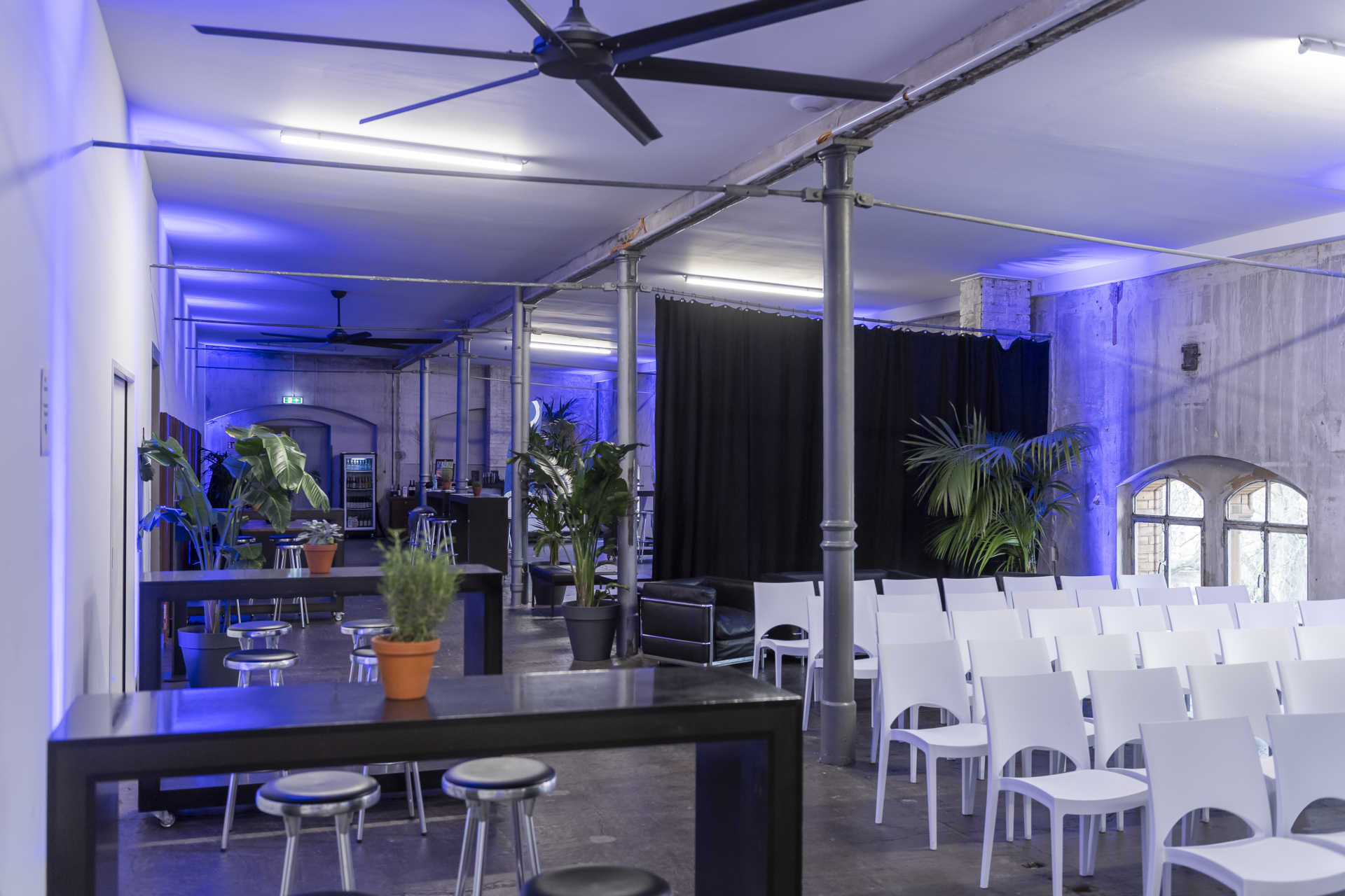Industrielle Loftetage mit Konferenzbestuhlung, Stehtischbrücken und blauen Lichtspots