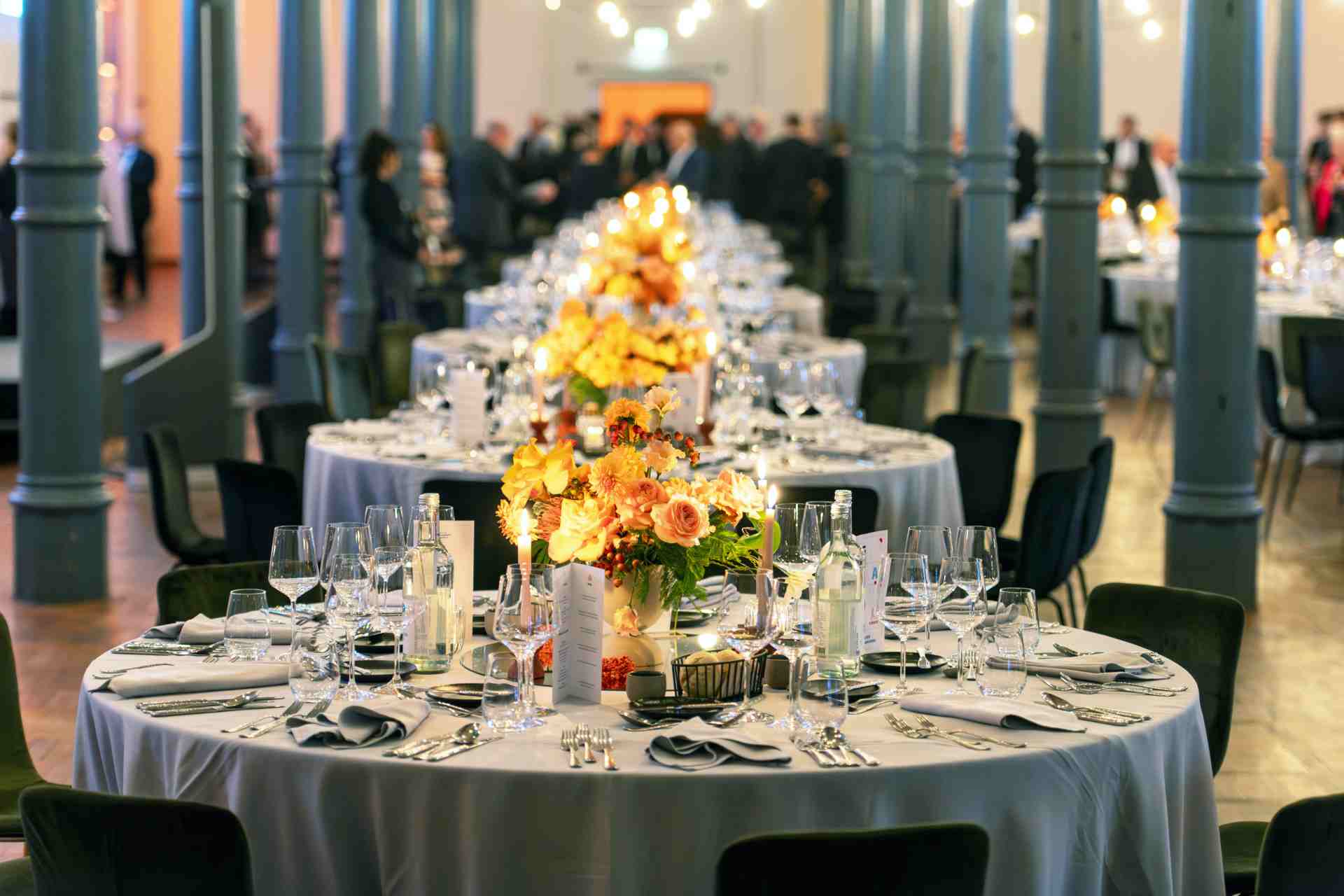 Festlich gedeckte Gala Tische, orange Blumen viele Gläser und Geschirr im Magazin der Heeresbaeckerei
